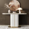 A luxurious white marble console table with a fluted pillar base and gold accents, styled with a vase of dried pampas grass, a decorative bowl, and a modern mushroom lamp against a muted wall with a large abstract round wall art piece.