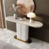 A luxurious white marble console table with a fluted pillar base and gold accents, styled with a vase of dried pampas grass, a decorative bowl, and a modern mushroom lamp against a muted wall with a large abstract round wall art piece.