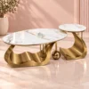 Designer Brass marble coffee table set with an oval centre table and round side table against a soft peach studio background.