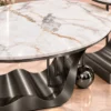 Close-up of oval white marble centre table top with grey and black veining, curved stainless steel base and decorative sphere.