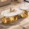 Elevated view of oval marble coffee table and matching round table with white veined tops and flowing gold metal bases.