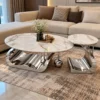 Designer oval marble centre table and matching round Chrome side table arranged beside a cream sectional sofa in a modern home.