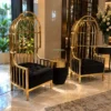 Two luxury gold birdcage accent chairs with black tufted seats and matching side table in an elegant marble-floored foyer