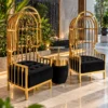 Pair of gold stainless steel lounge chairs with arched birdcage frames and black cushioned seats in a luxury atrium.