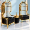Pair of modern gold stainless steel accent chairs with domed birdcage backs, black tufted cushions and matching table against a light blue wall.