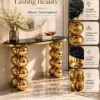 Gold sphere console table with black marble top and stainless steel construction, shown in an Alliance International product features graphic.