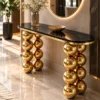 Angled view of a luxury gold sphere console table with polished black marble top and sculptural stainless steel supports.