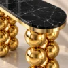 Close-up of polished black marble console tabletop with white veining, gold stainless steel edging and reflective spherical legs.