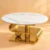 Luxury round marble centre table with polished gold stainless steel S-curve base against a warm creamy background.