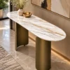 Designer oval marble console table with two curved bronze stainless steel pedestal supports against a contemporary entryway wall.
