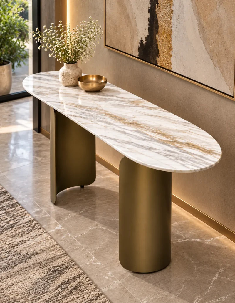 Designer oval marble console table with two curved bronze stainless steel pedestal supports against a contemporary entryway wall.