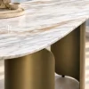 Close-up of white marble console tabletop with grey and gold veining above two curved bronze-gold stainless steel supports.