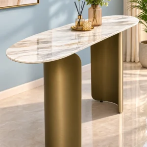 Modern oval marble console table with curved bronze stainless steel pedestal base styled with a vase and decorative tray against a pale blue wall.