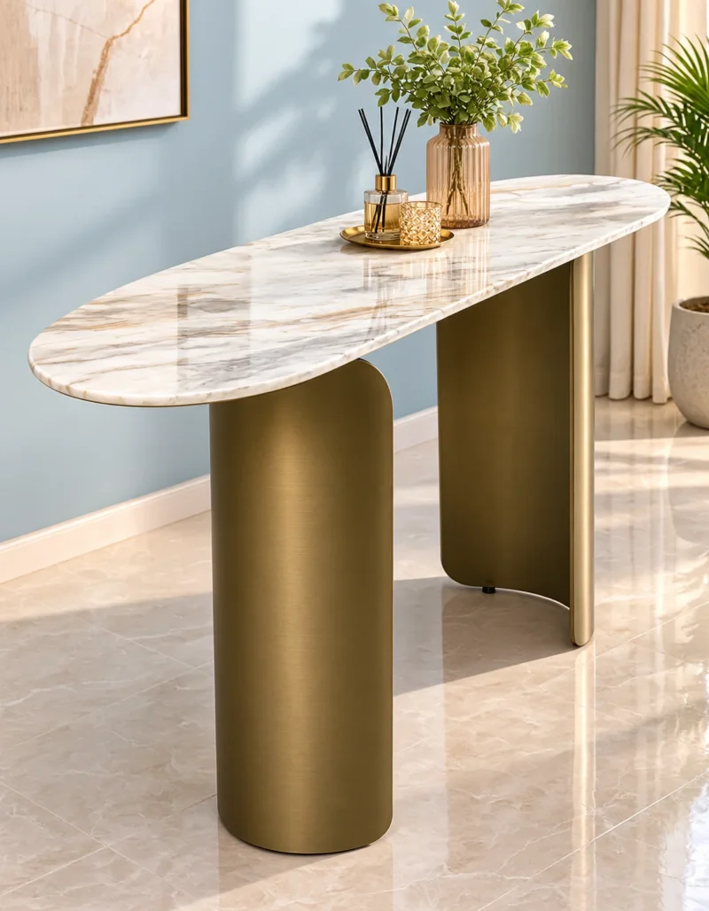 Modern oval marble console table with curved bronze stainless steel pedestal base styled with a vase and decorative tray against a pale blue wall.