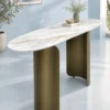 Oval white marble entryway console table with bronze-gold cylindrical and curved metal supports in a minimal light-blue interior.
