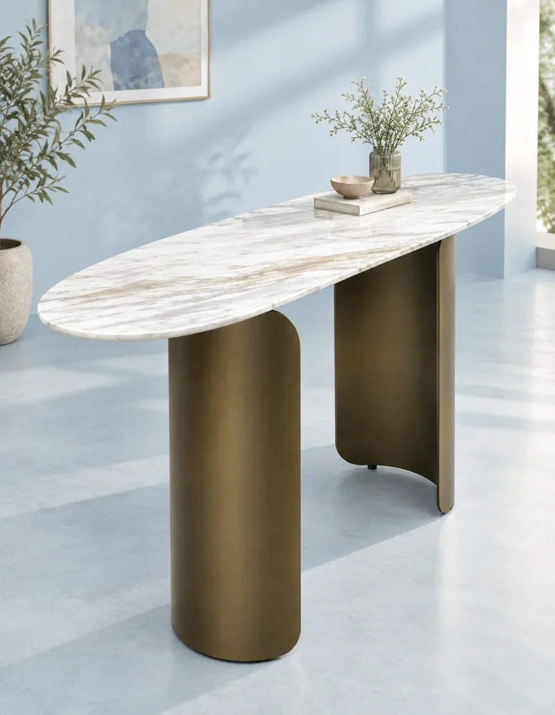 Oval white marble entryway console table with bronze-gold cylindrical and curved metal supports in a minimal light-blue interior.