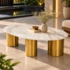 Luxury oval marble centre table with three gold cylindrical legs, styled with a ceramic vase beside a modern outdoor lounge.