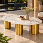 Luxury oval marble centre table with three gold cylindrical legs, styled with a ceramic vase beside a modern outdoor lounge.