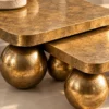 Close-up of antique-gold marble nesting centre table tops with rounded edges and textured gold stainless steel sphere legs.