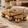 Designer gold sphere nesting centre table set styled with a flower vase and decorative books in front of a cream living room sofa.