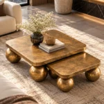 Elevated view of two square antique-gold nesting centre tables with rounded corners and stainless steel ball-shaped supports.