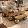 Gold marble coffee table set of two with spherical stainless steel legs in a luxury lounge with beige sofa and accent chair.