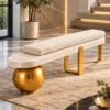 Designer bouclé bench with ivory cylindrical cushion and sculptural gold stainless steel base near a modern staircase.