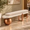 Modern ivory bouclé bench with elongated upholstered cushion, cream platform and copper sculptural supports in a luxury living room.