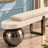 Close-up of textured ivory bouclé bolster cushion, rounded cream bench platform and polished black spherical support.
