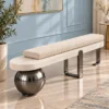 Luxury upholstered bouclé bench with ivory cylindrical cushion and gun metal stainless steel supports against a pale blue wall.