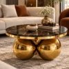 Luxury round centre table with black marble top and gold sphere base positioned in front of a beige sofa.