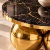 Close-up of black marble tabletop with gold veining, polished gold metal edge and reflective stainless steel sphere base.