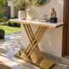 Luxury white marble console table with intersecting gold stainless steel X base styled with flowers beneath a round mirror beside a garden.