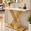 Gold stainless steel console table with white marble top, geometric crossed rod base and decorative vase beneath a circular mirror in a luxury living room.