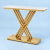 Modern rectangular white marble console table with sculptural gold stainless steel X-shaped rod base against a light blue background.