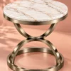 Avenza Luxe round marble side table with sculptural hourglass stainless steel frame against a peach background