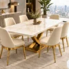 Modern 6 seater marble dining table with gold X pedestal beside large city-view windows