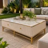 White marble coffee table with gold stainless steel legs and ribbed white body styled beside a cushioned sofa on a garden patio.