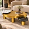 Luxury gold centre table with white and black marble accents displayed in front of a curved cream sofa in a modern living room.