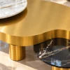 Close-up of brushed gold stainless steel centre tabletop with curved edge, raised white marble accent and black marble side surface.