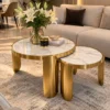 White marble nesting centre table set with gold stainless steel legs in front of a beige sectional sofa and white lilies.