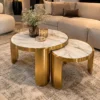 Round marble centre table set of two with white gold-veined tabletops and curved gold stainless steel legs beside a cream sofa.