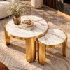 Elevated view of two white marble nesting coffee tables with gold rims, grey veining and curved stainless steel legs.