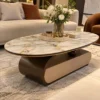 Luxury oval marble centre table with bronze curved base and gold edge accents in front of a cream living room sofa.