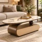 Modern oval marble centre table with gold-trimmed tabletop and curved bronze base beside a beige sofa.