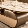 Close-up of white marble centre table with grey and gold veins, gold edge trim and curved stainless steel base.