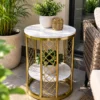 Two-tier gold marble side table beside a woven patio chair and surrounding greenery