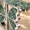 Close-up of emerald-green marble console tabletop with white veining and silver stainless steel butterfly-wing detailing.