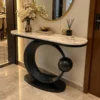 Luxury marble console table with black circular steel base styled beneath a round mirror in an entryway.