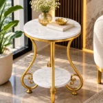Round white marble side table with gold curved legs and lower shelf positioned near a modern living room window